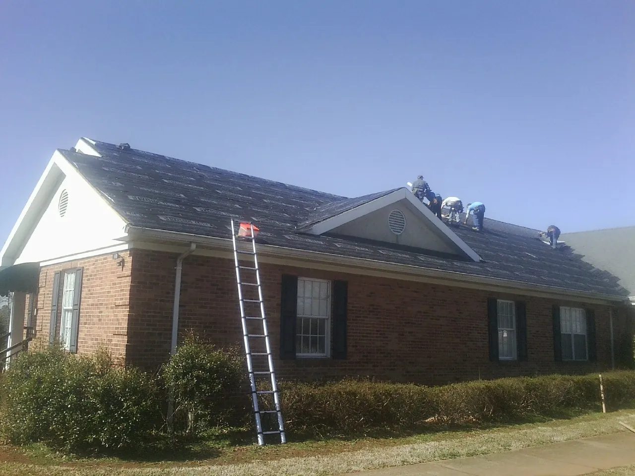 Crew tearing shingles off a brick ranch roof with a ladder set — Emergency Roof Repair work by our crew in Montour