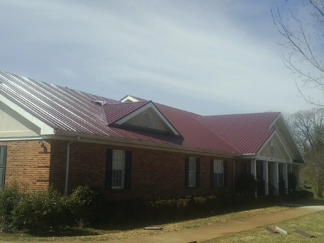 Red metal roof with gabled entries on a long brick building, from a Hail Damage Roof Repair job in Montour