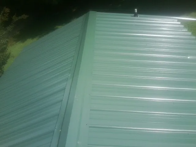 New green metal panels meeting at the ridge of a roof — Flat Roof Repair work by our crew in Montour
