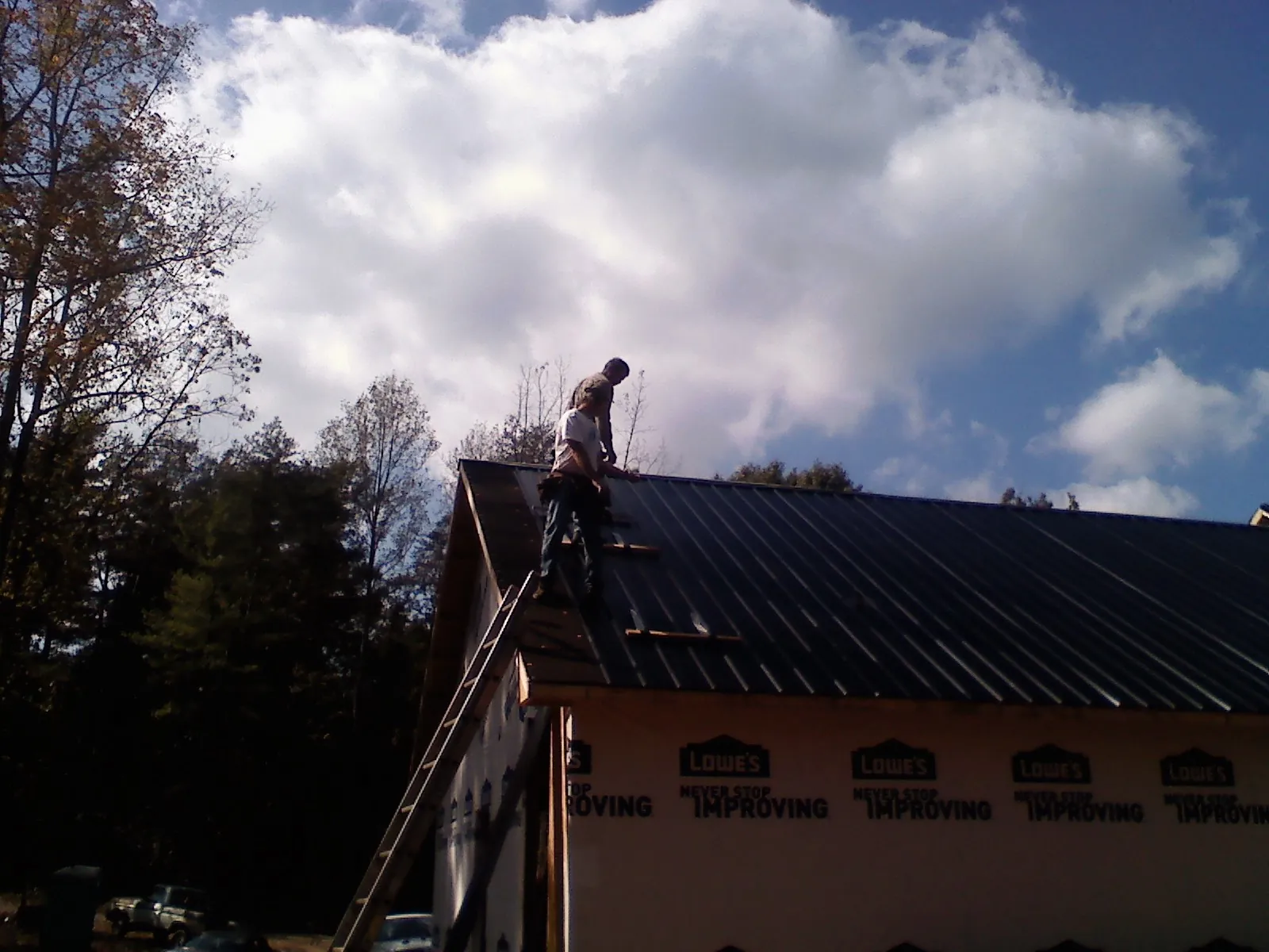 Roofer fastening dark metal panels high against a cloudy sky, from a Roof Inspection job in Montour