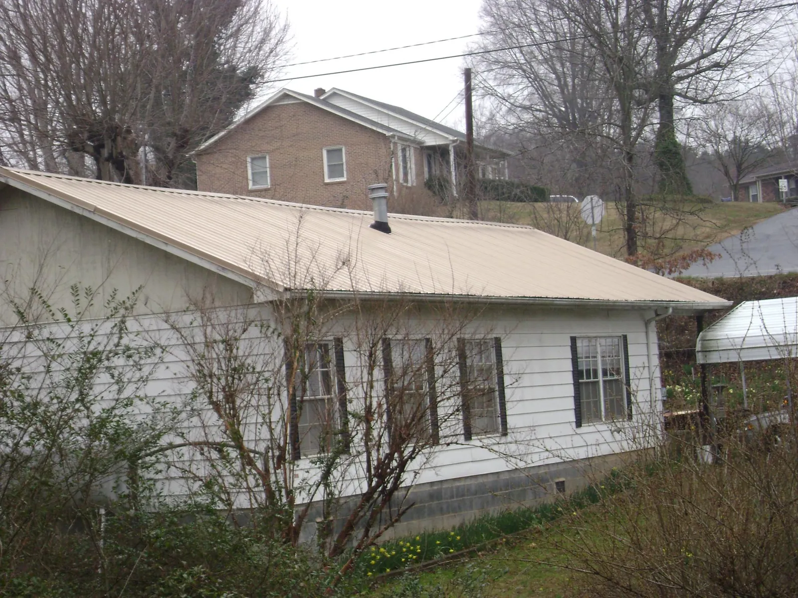 Tan metal roof on a white sided house set into a hillside — Commercial Roofing by Roofing Brothers in Montour