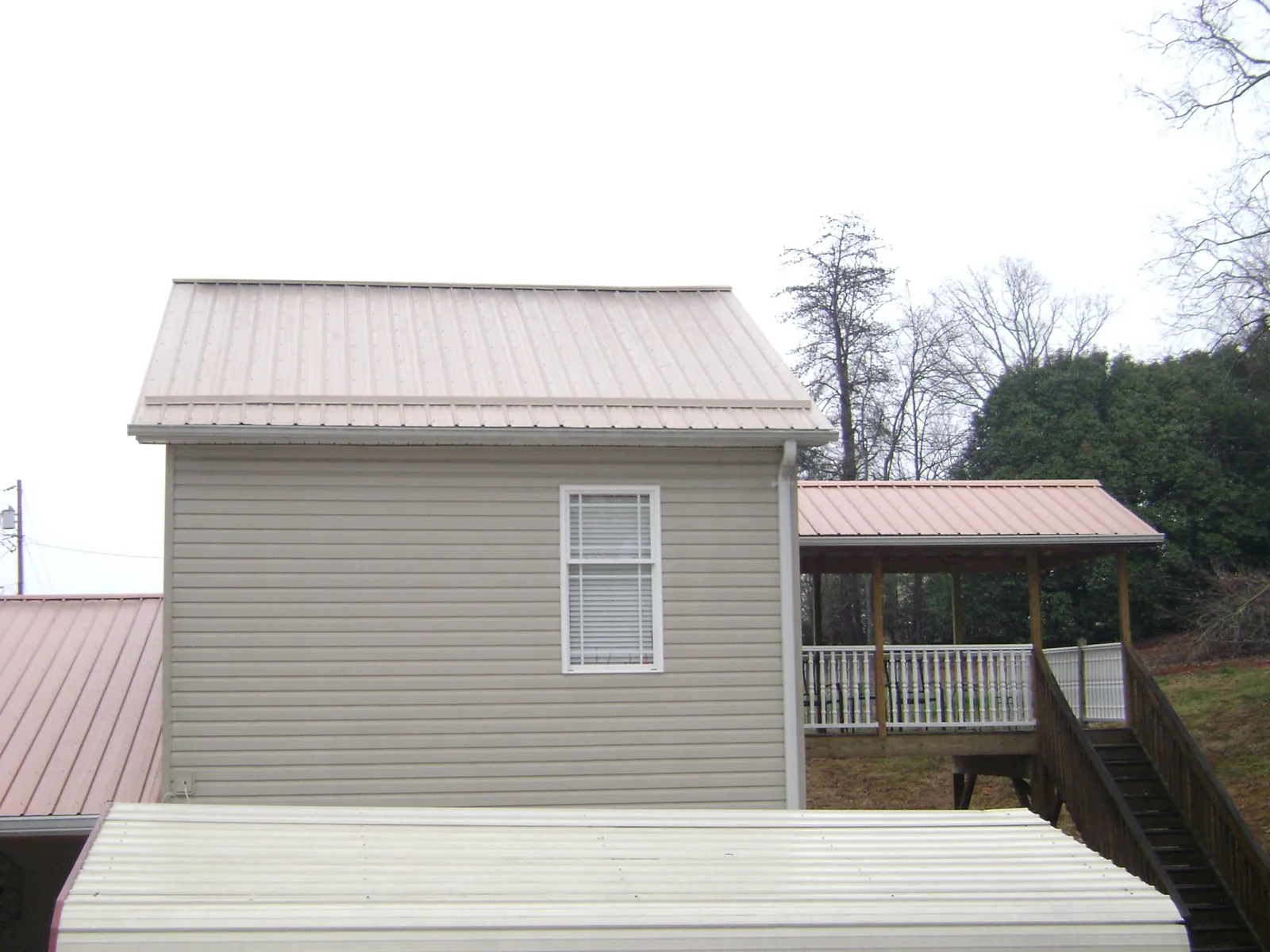 Tan metal roofs on a two story addition and attached porch, from a Roof Replacement job in Montour